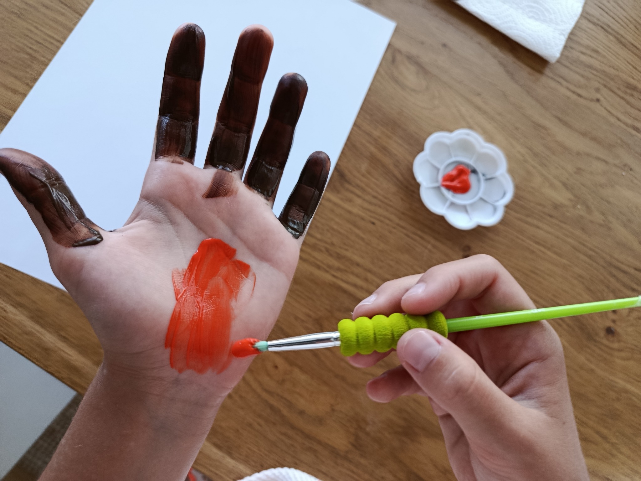 Una mà amb els dits marrons rep pintura taronja al palmell.